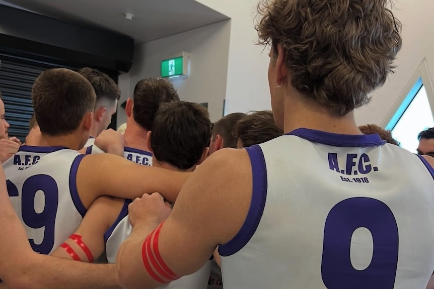 A group of male footballers huddled together wearing red armbands