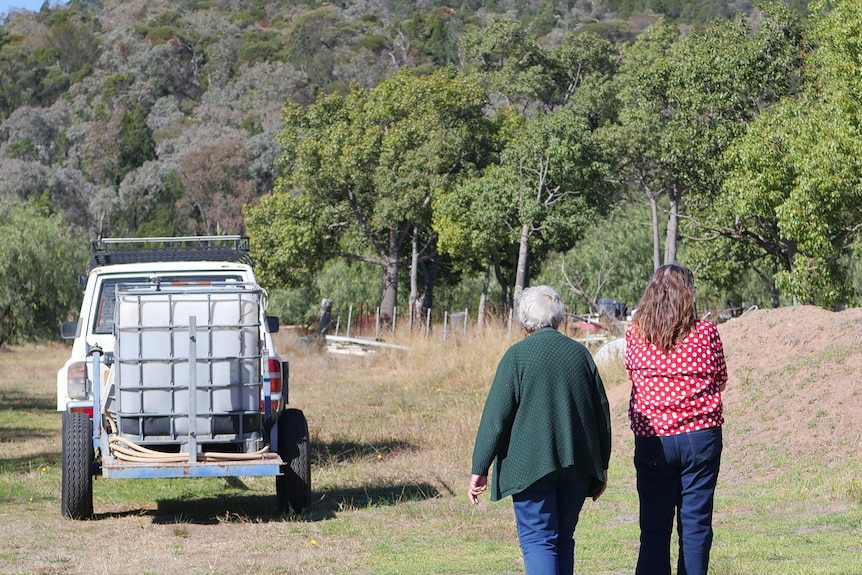 Two women walk towards an old car with sprayer on back.