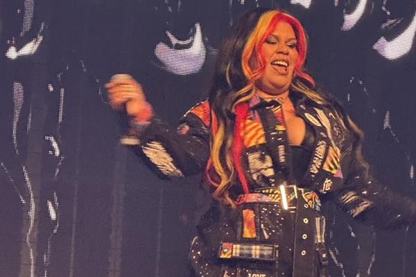 Barkaa on stage with hair the colours of the Aboriginal flag, holding mic, dancing.