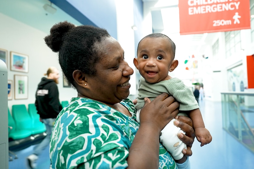 A Papua New Guinean woman smiles while looking at and holding her baby son.