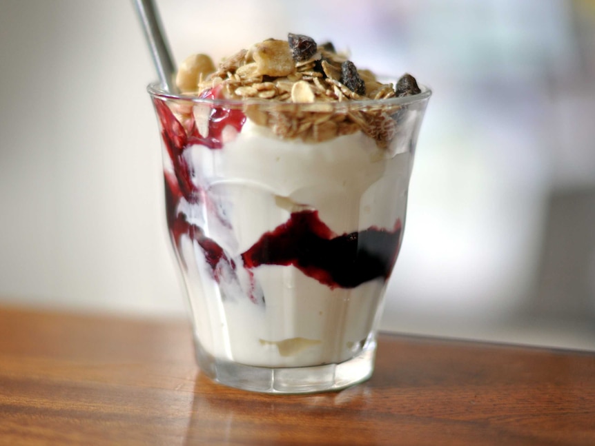 A yoghurt and berry parfait in a small glass, with a spoon in it.
