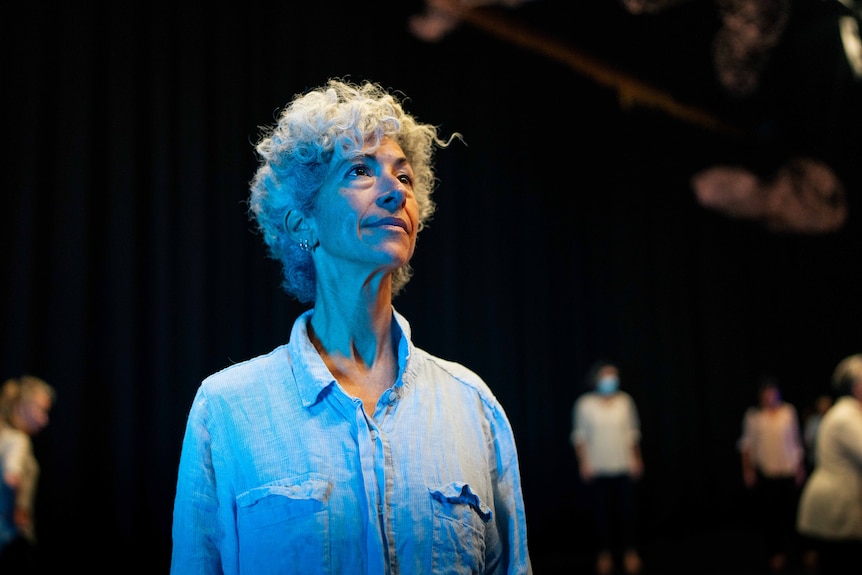 Woman with short grey hair looks out to distance in a dance studio