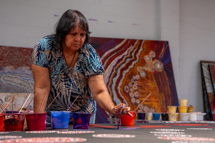 Artist Sandra Pumani leans over a canvas painting