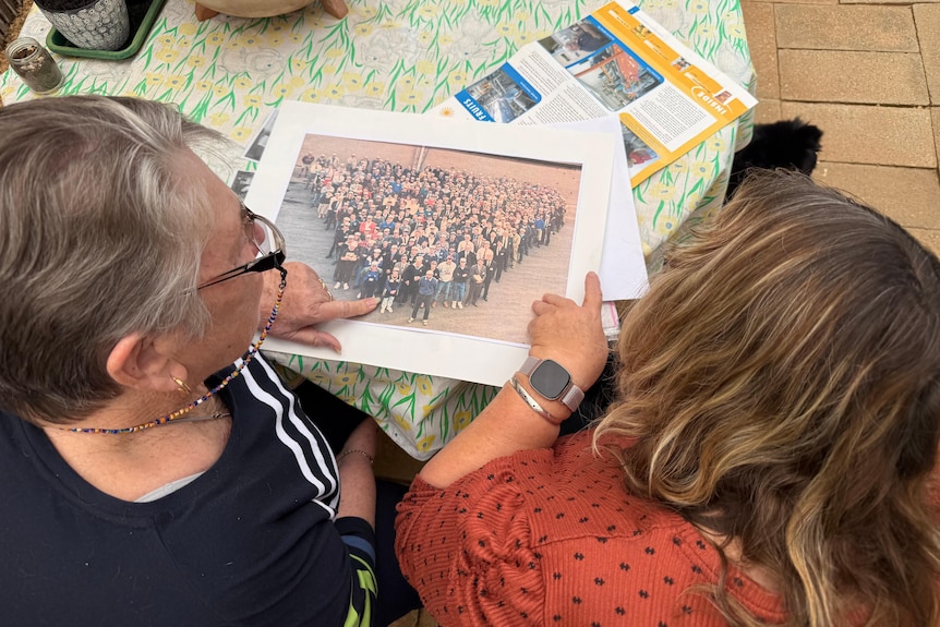 Two women look at an old group photo on a table
