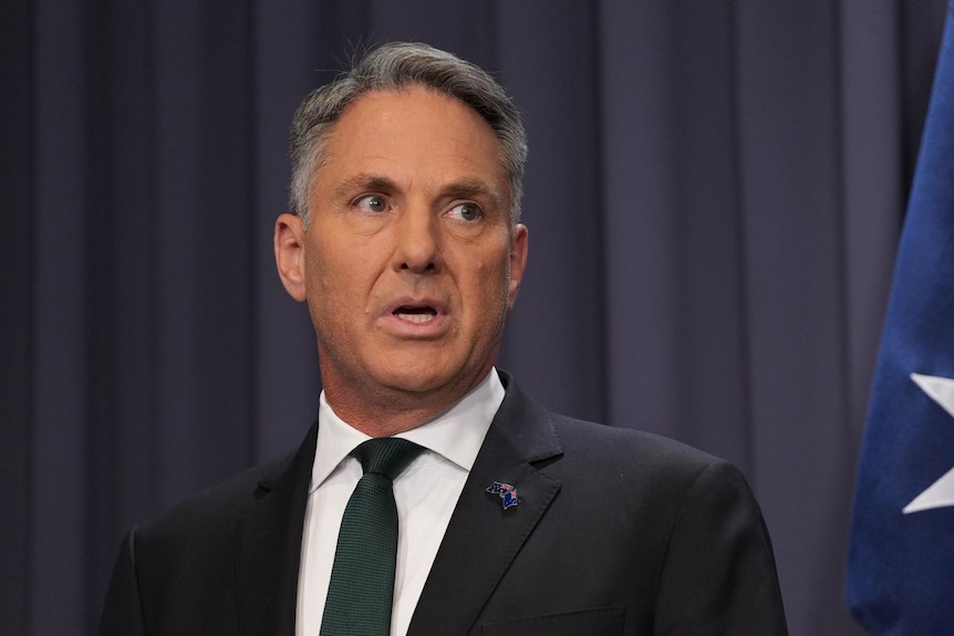 A man in a suit speaks at a press conference.