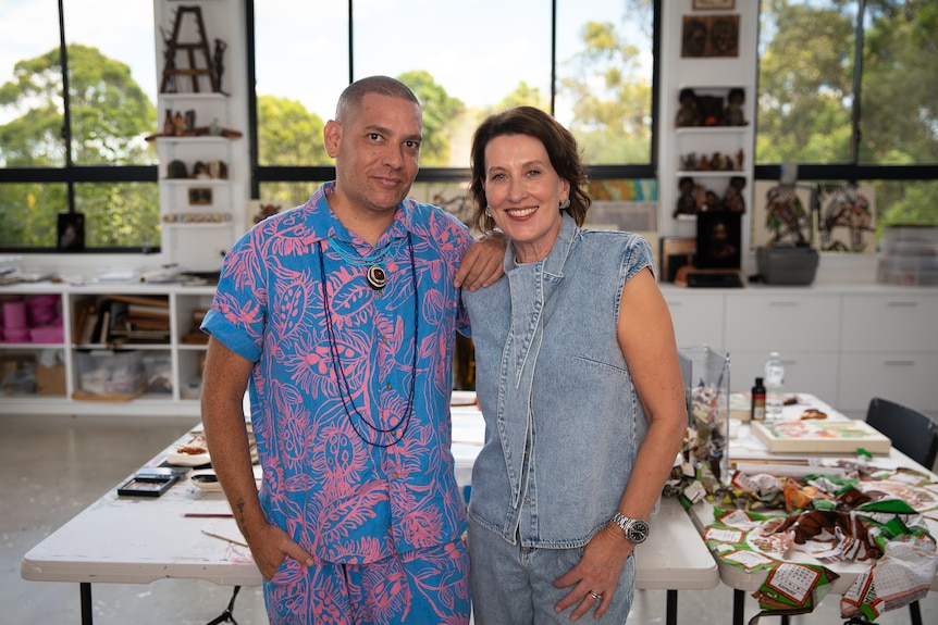Tony Albert and Virginia Trioli stand close together. Both look straight ahead smiling.