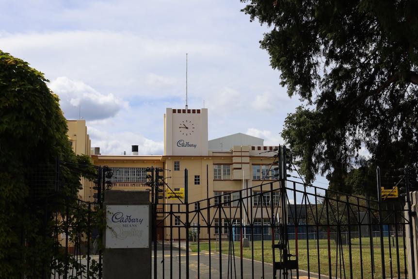 The Cadbury factory behind a locked metal gate. View of the side of the building with a clock and flagpole on top