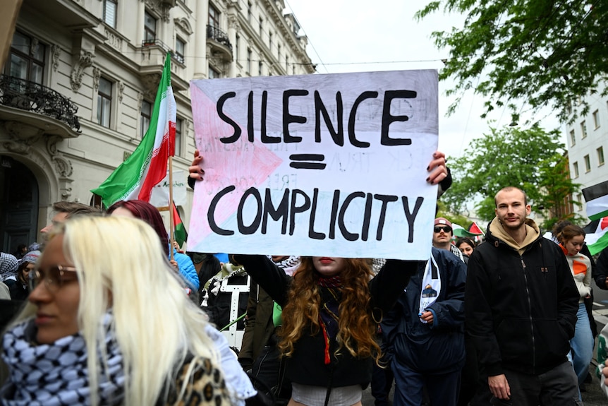 Protesters hold a sign that says silence = complicity