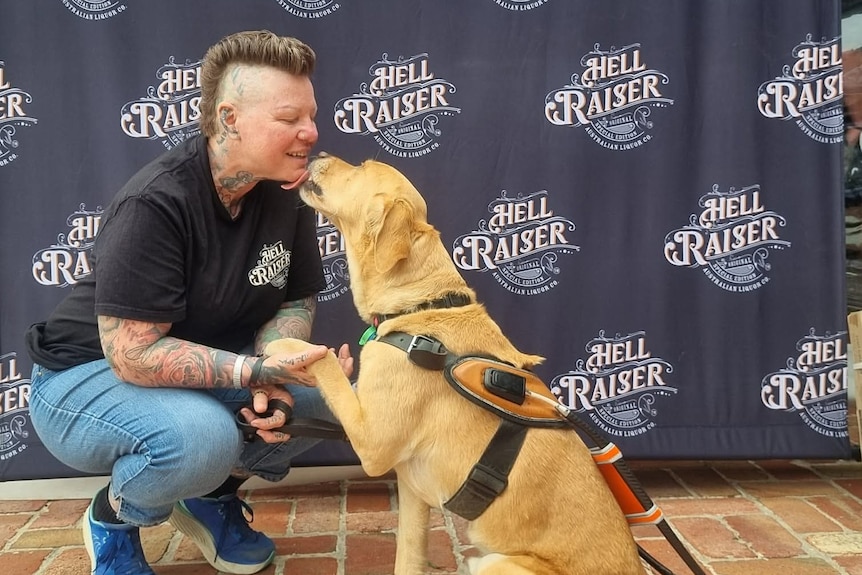 A woman squats down while a dog puts his paw up and tries to lick her