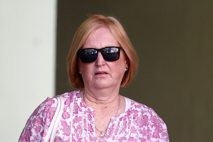 A woman with sunglasses and wearing a pink and white shirt.