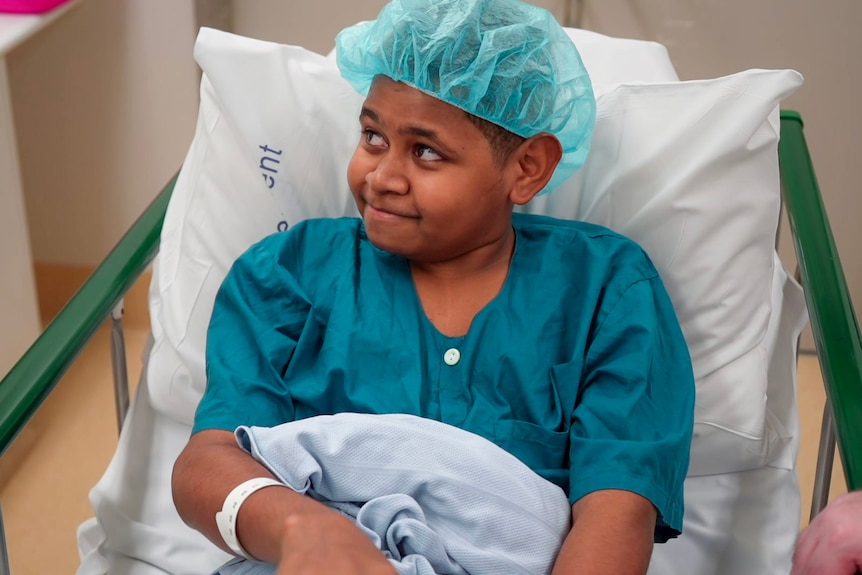 A boy in hospital gown and cap in a hospital bed