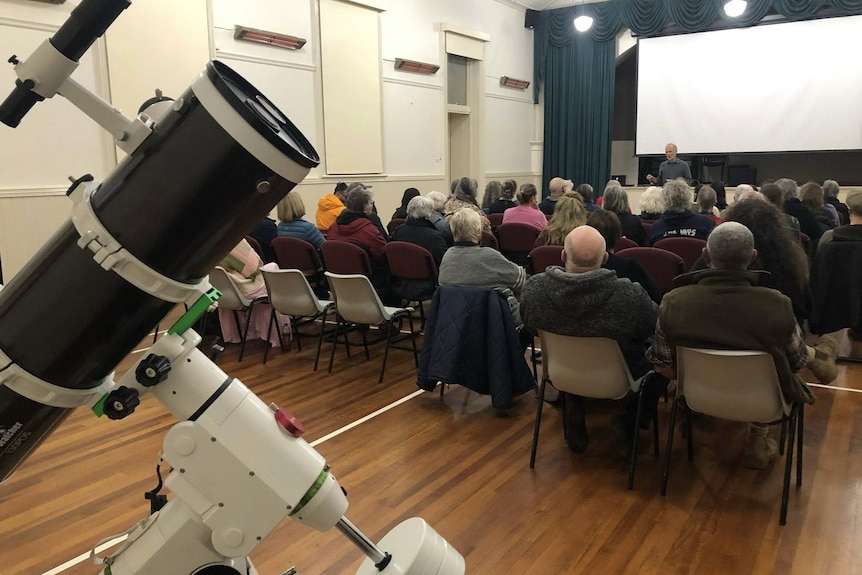 A room filled with people, a telescope in the foreground.