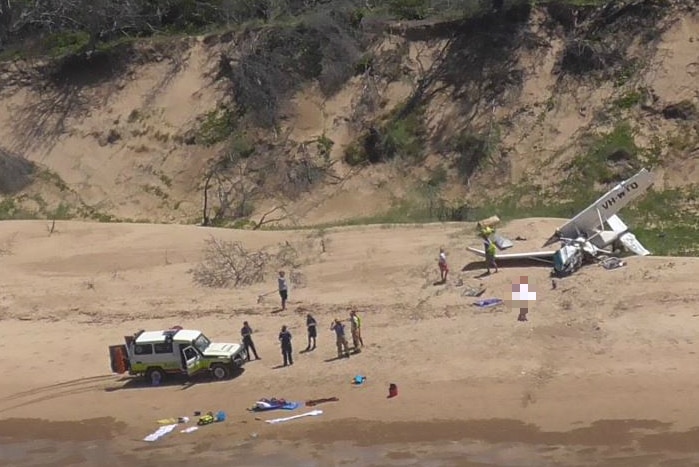An aerial view of a crashed plane, people and a four-wheel-drive on a beach.