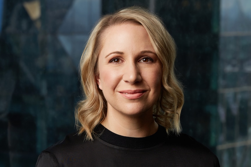 a woman with blonde hair and a black shirt looks at the camera