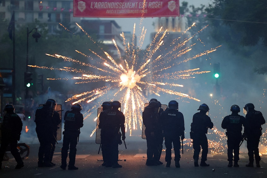 Police are silhouetted as a firework explodes on a Paris street.