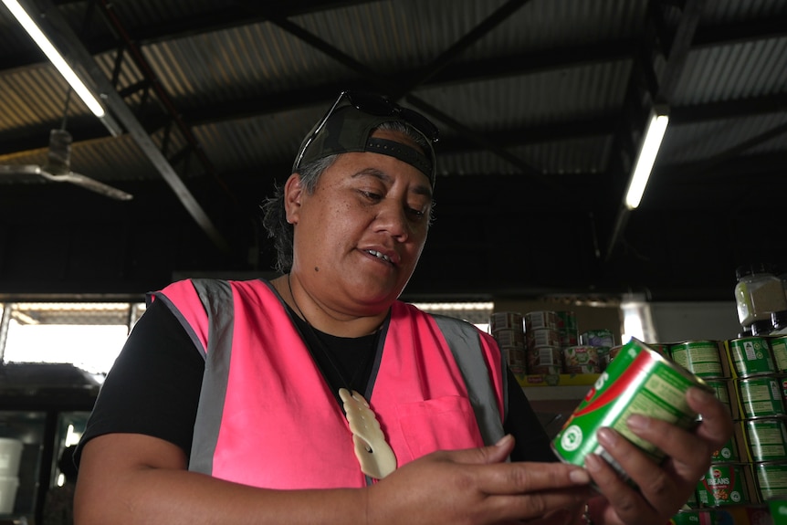 A woman in a high-vis vest looking at a can of baked-beans.