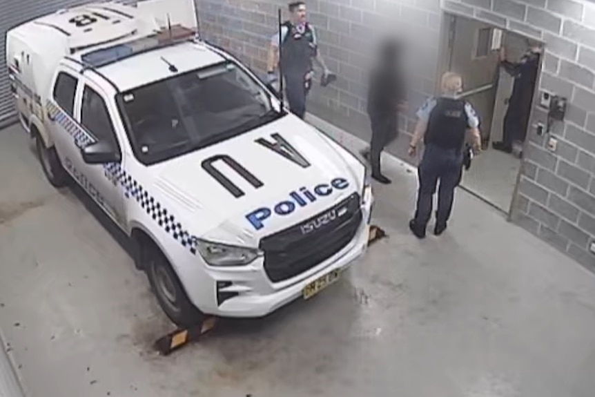 A handcuffed man at a police loading dock.