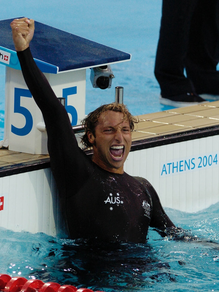 Mid-scream, Ian Thorpe triumphantly raises his fist in the air as he stand at the end of a pool.