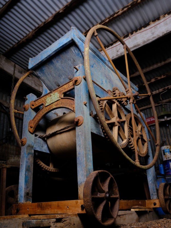 The cider mill sits in a garage with rusted metal and a light blue wooden frame around it.