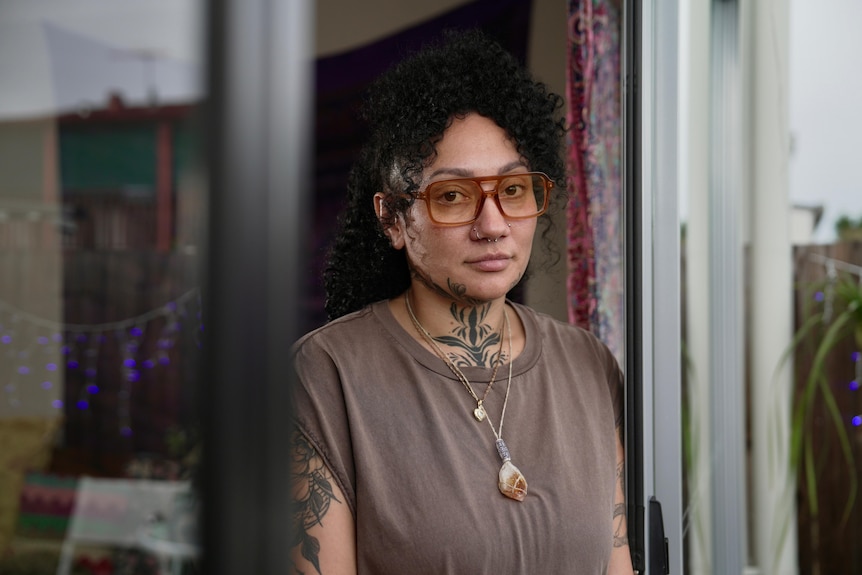 Woman with black curly hard and yellow glasses looking out a window frame