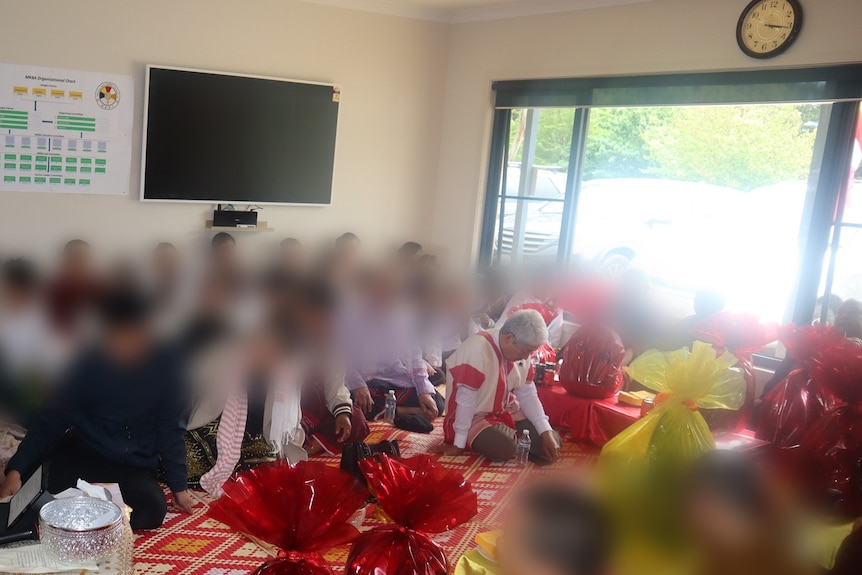 A man sitting amongst a large gathering of people who have all been blurred out.