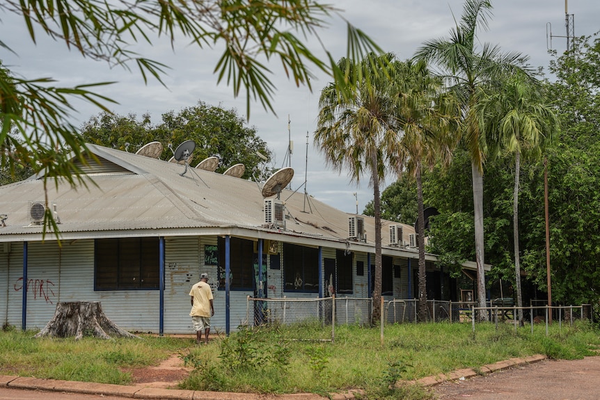 A man walking towards a tin building with palm trees along the side. 