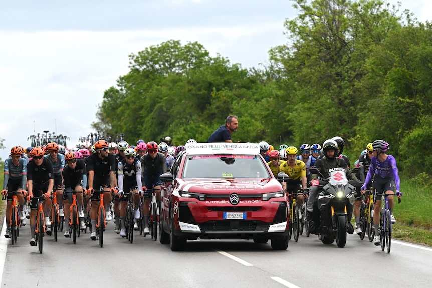 The peloton rides behind a car