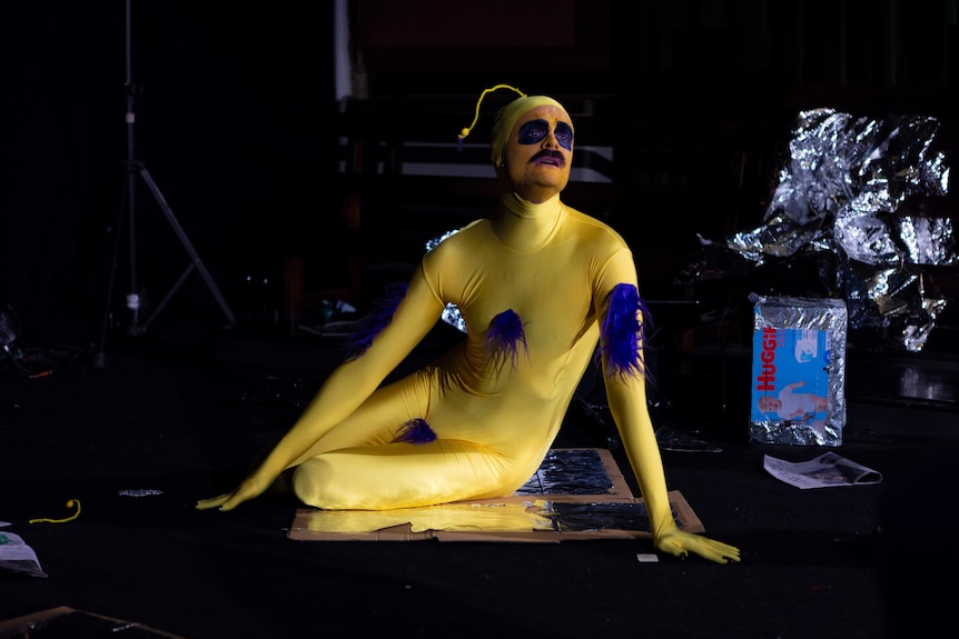 A man wearing a yellow and purple costume performs on stage.