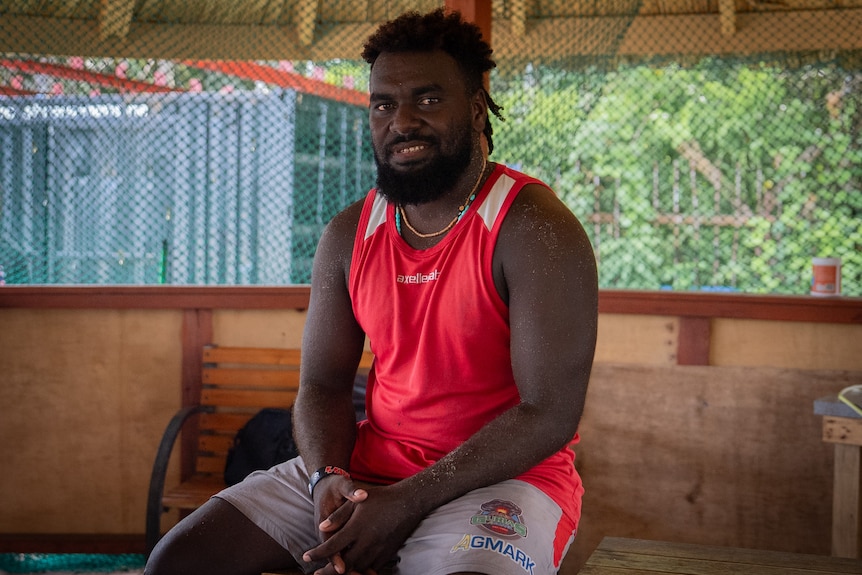 A photo of Solomon Semoso wearing a red rugby jersey and smiling.