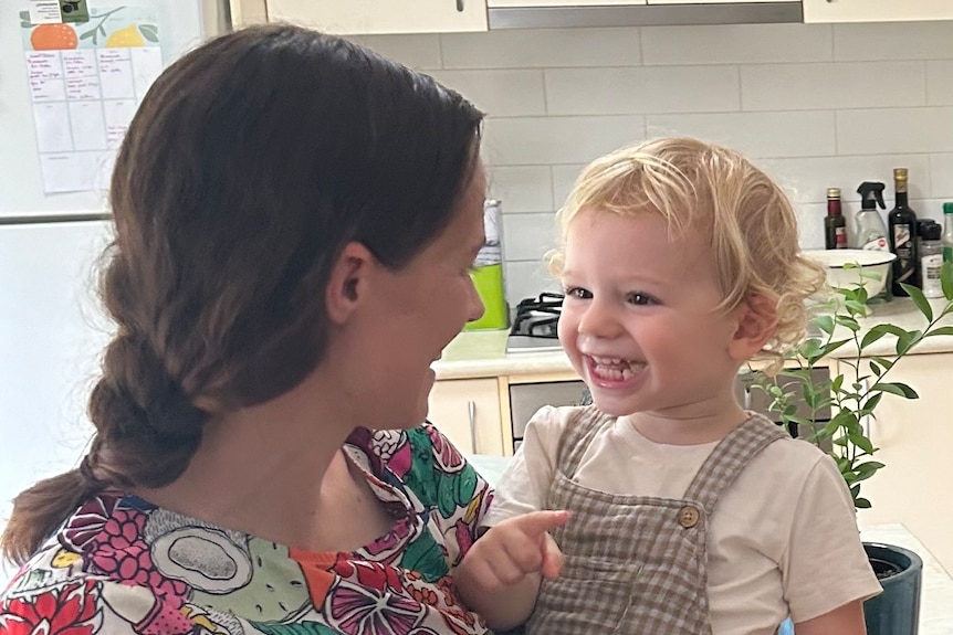 A smiling woman holding her smiling son in a house with a white kitchen in the background