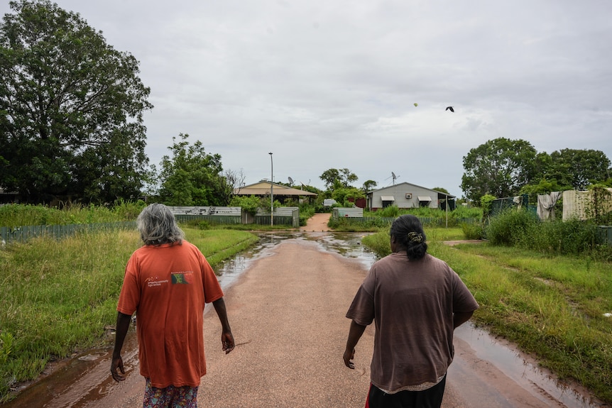Two Aboriginal women walking away from camera down a road