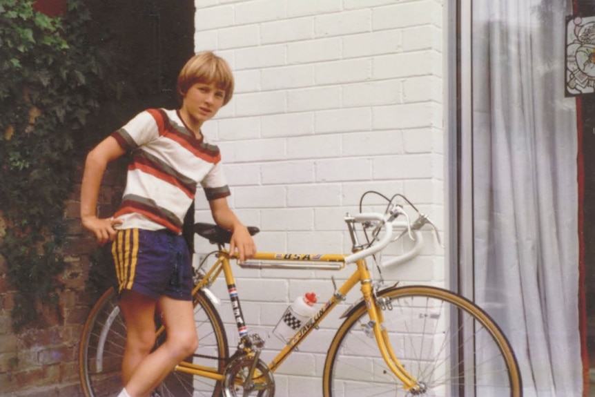 Boy in striped shirt with bicycle near brick wall.