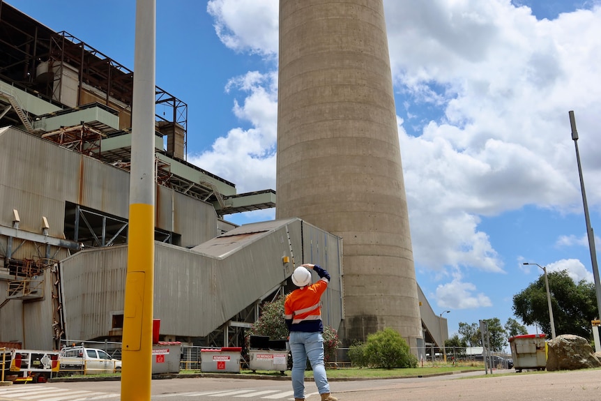 A worker looks up at a pair of huge smoke stacks at an industrial site.