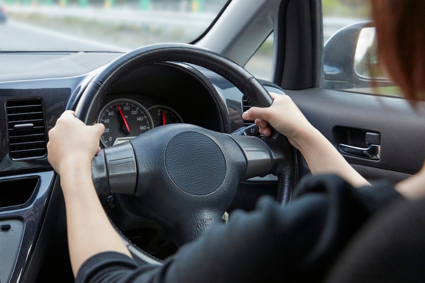 Backseat view of a woman driving a small car.