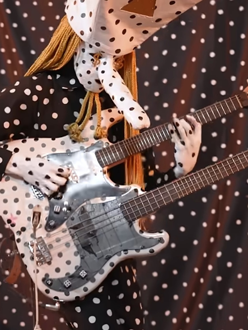 A person in costume plays a double-necked guitar and bass.