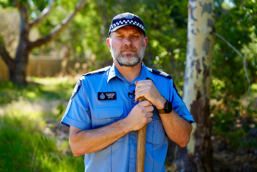 A police officer standing behind a tree.