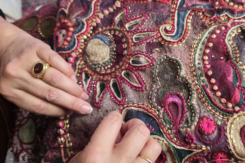 A close up of hands on an embroidered quilt.