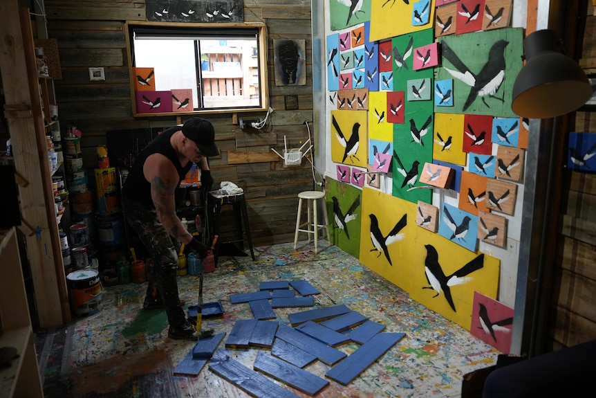 Mike Mclean in his Torquay studio using a roller to paint the background of his popular willy wagtails.
