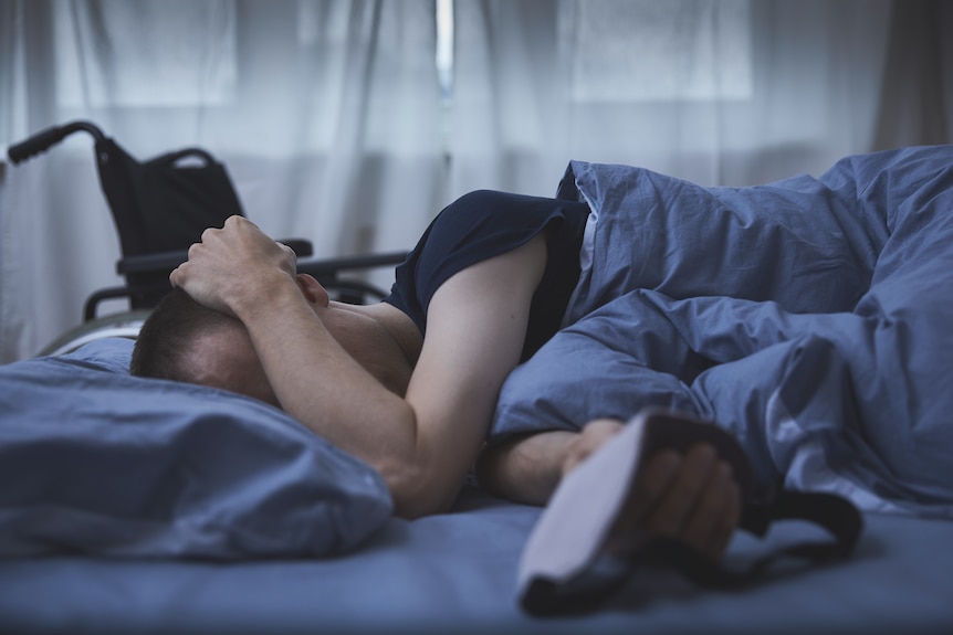 A person lays in bed with their hand over their face.