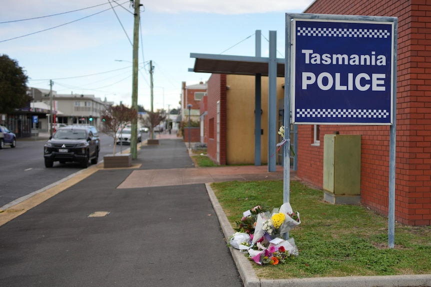 Flowers placed in tribute at the foot of a Tasmania police sign outside a police station.