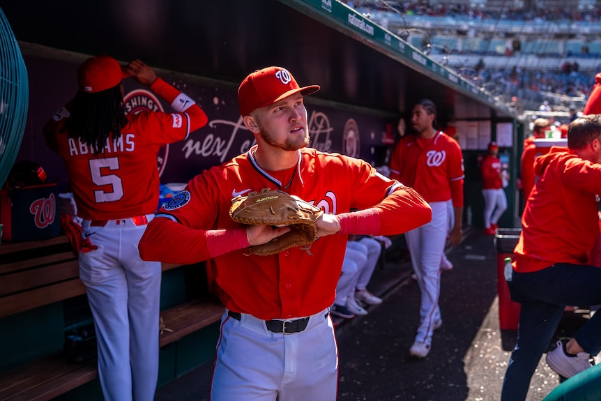 Curtis Mead, wearing a red kit and a pitcher's mitt, standing in the dugout during a baseball game.