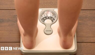 A generic image of a person standing on a pair of silver weight scales. You can see their bare legs and feet.