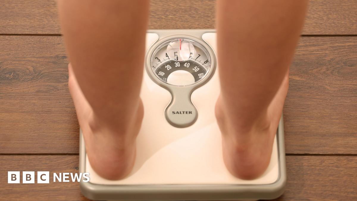 A generic image of a person standing on a pair of silver weight scales. You can see their bare legs and feet.
