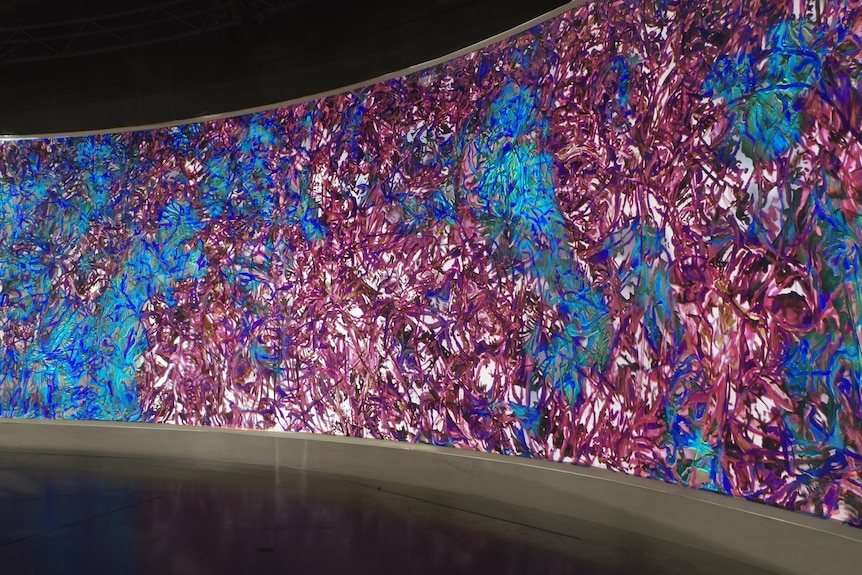A large, curved video screen, with an intricate, bright pink and blue pattern moving on it.