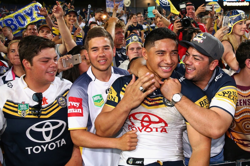 Jason Taumalolo celebrates with fans after winning a grand final as teammates surround him. All smiling.