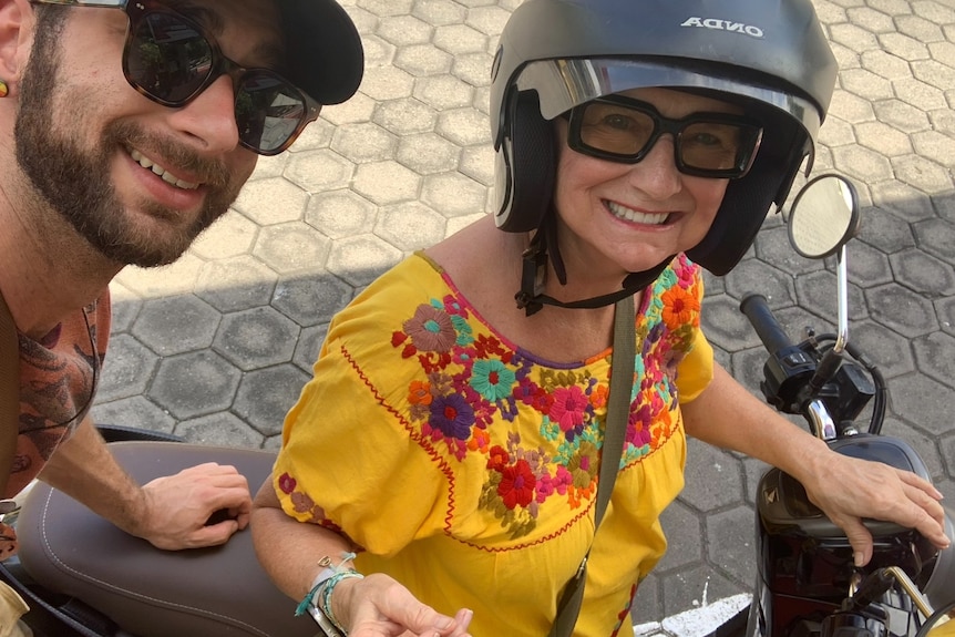 A middle aged woman leaning on a motorbike, smiling