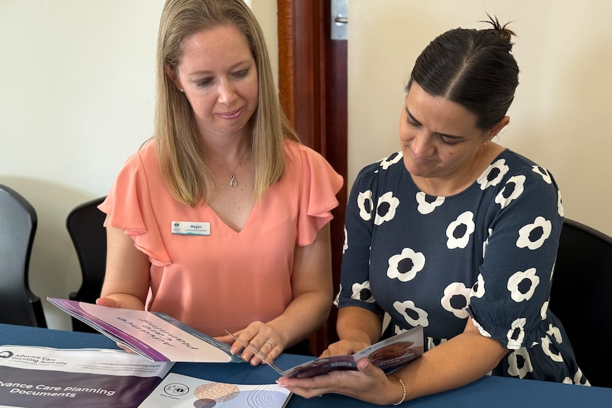 Two women sit at a table as they look at information pamphlets and brochures.