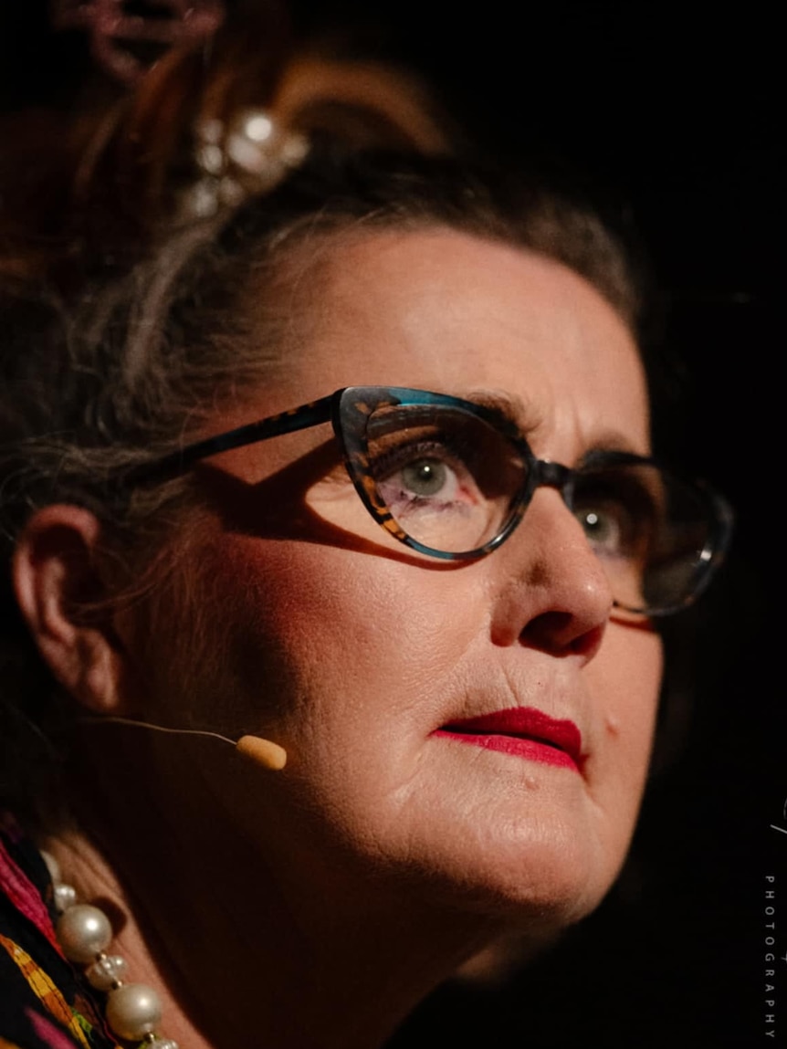 Woman with glasses, red lips, and a microphone taped to her face.
