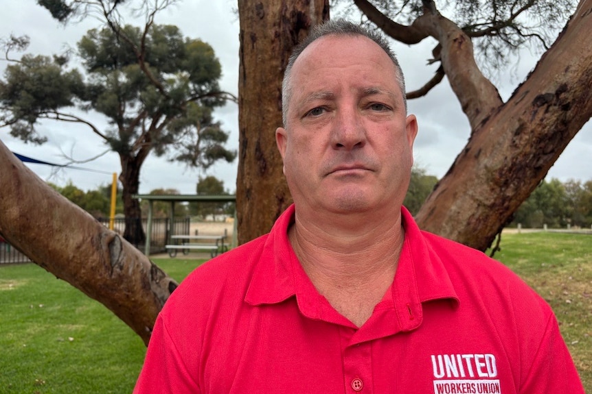 A man wearing a red t-shirt looks sternly at the camera.