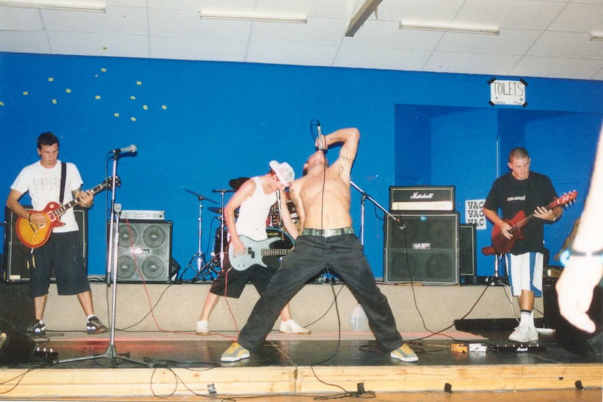 Four male members of rocka band on stage with blue background